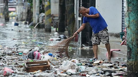 A man cleans garbage along a flooded street due to Typhoon Fung-wong and high tide on Monday, Nov. 10, 2025, in Navotas, Philippines.