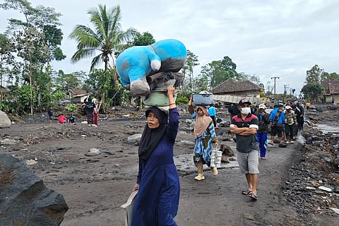 People carry their belongings as they evacuate their homes at a village affected by the eruption of Mount Semeru in Lumajang, East Java, Indonesia, Thursday, Nov. 20, 2025.