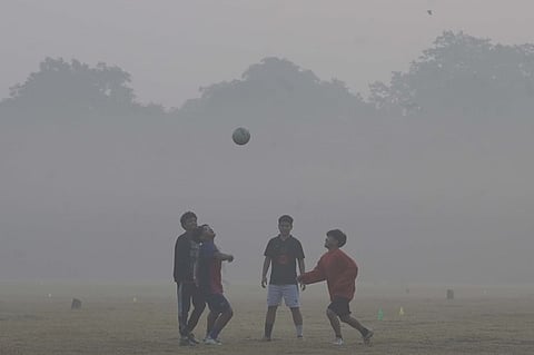 Youths play football amid air pollution smog at a garden in New Delhi