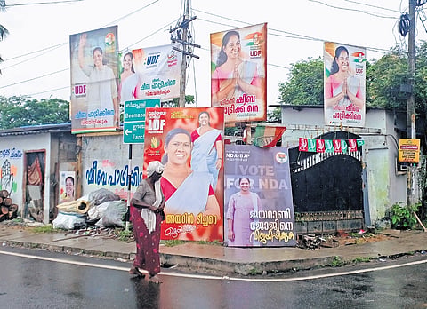 A woman walks past a bunch of flex boards of candidates fielded by various political fronts at Valiyathura in Thiruvananthapuram