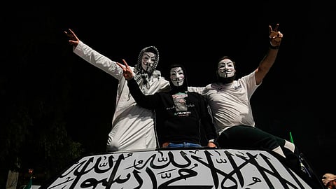Syrian men wearing anonymous masks flash victory signs, as they stand on top of their car with its front window covered by an Islamic flag, during celebrations marking the first anniversary of the ousting of the Bashar Assad regime in Damascus, Sunday, Dec. 7, 2025.