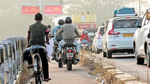 Following heavy traffic congestion on the Goshree bridge, commuters ride through the footpath, violating traffic rules, to reach their destination on time.