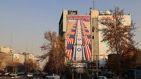 Iranians drive past an anti-US and anti-Israel billboard displaying a message from the Secretary of the Supreme National Security Council that reads “Watch out for your soldiers” following a social media post by the US president supporting anti-government protests in Tehran on January 4, 2026.