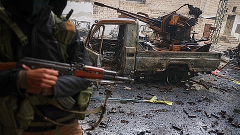 A member of Syrian security forces stands next to a destroyed vehicle in the predominantly Kurdish Sheikh Maqsoud neighborhood where clashes broke out Tuesday, Jan. 6