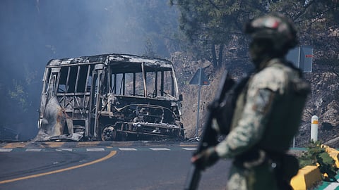 A soldier stands guard by a charred vehicle after it was set on fire, in Cointzio, Michoacán state, Mexico, Sunday, Feb. 22, 2026, following the death of the leader of the Jalisco New Generation Cartel, Nemesio Oseguera, known as "El Mencho."
