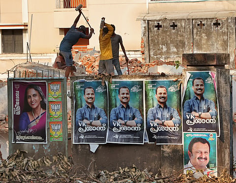 Migrant workers dismantle a structure amid piles of debris near a wall layered with rival campaign posters at Kowdiar in Thiruvananthapuram on Thursday.