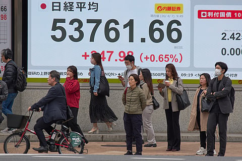 People stand in front of an electronic stock board showing Japan's Nikkei index at a securities firm Tuesday, April 7, 2026, in Tokyo.