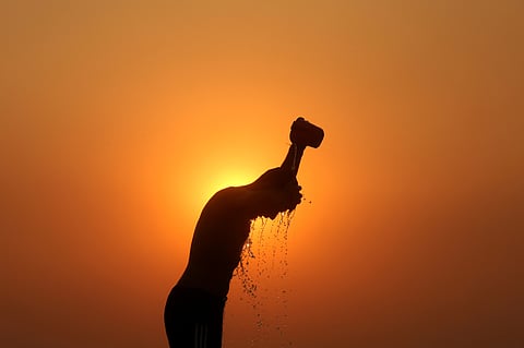 A labourer is silhouetted against the setting sun as he bathes on a hot summer day.