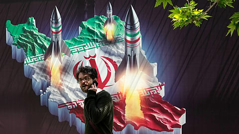 A passerby, taking his cellphone, walks past a banner showing missiles being launched from an Iranian map in northern Tehran, Iran, Friday, April 19, 2024.