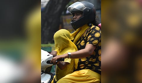 A woman covers the baby with a scarf as they travel on a sunny day in Vijayawada on Friday.