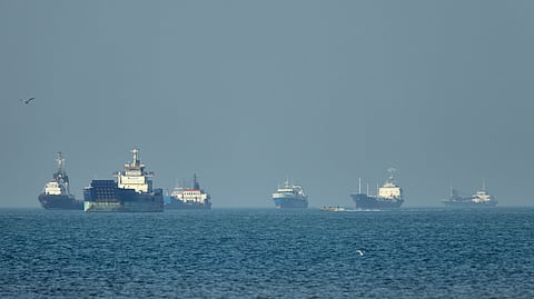 Cargo ships, including bulk carriers and general cargo vessels, sit at anchor offshore as a small motorboat passes in the foreground, in the Strait of Hormuz off Bandar Abbas, Iran, Monday, May 4 , 2026.