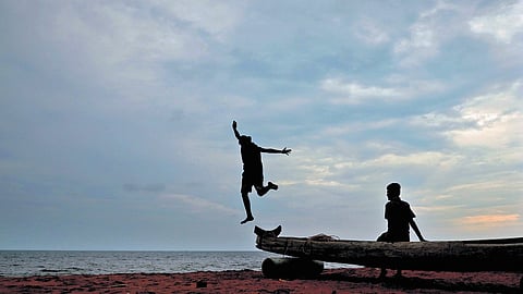 A boy jumps off a traditional catamaran at Veli Beach in Thiruvananthapuram under cloudy skies following a rain alert by IMD