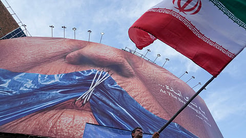 A man waves an Iranian flag for a pro-government campaign under a billboard with graphic showing Strait of Hormuz and sewn lips of U.S. President Donald Trump in a square in downtown Tehran, Iran, Wednesday, May 6, 2026