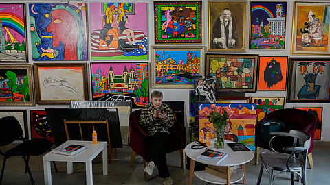 A gallery attendant sits in an armchair near the wall covered with paintings by Ukrainian artists at the Art Kyiv 2026 Festival at the Art Ukraine Gallery in Kyiv, Ukraine, Friday, May 8, 2026. (
