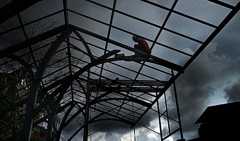 A worker hurriedly engaged in construction work of a waiting shed against the backdrop of dark rain cloud