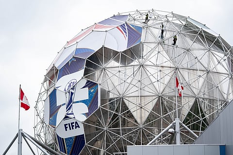 Workers drop from the top of Science World to install a football wrap for the 2026 FIFA World Cup football tournament in Vancouver, British Columbia, Wednesday, May 13, 2026.