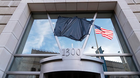 The American flag flying alone beside an empty flagpole that previously had the flag of the US Agency for International Development, or USAID, are pictured in the reflection of a window that previously had the sign and the seal of USAID, outside the agency's headquarters in Washington, Feb. 7, 2025.