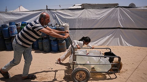 Ne'man Abu Jarad and his daughter push a cart loaded with jerrycans filled with water as they walk at a tent camp for displaced Palestinians in Khan Younis, southern Gaza Strip, Wednesday, May 13, 2026.