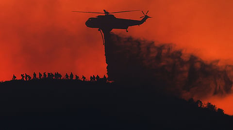 A water tanker drops water while firefighters walk below, as the Sandy Fire approaches, Tuesday, May 19, 2026, in Simi Valley, California.