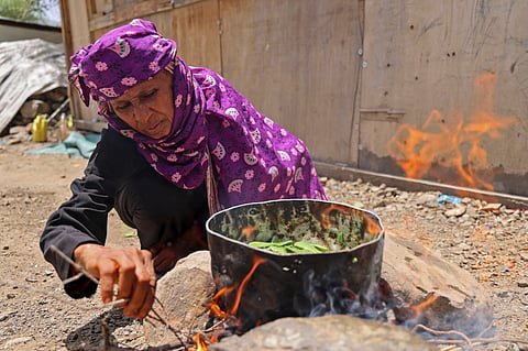 Displaced Yemeni woman Saeedah Mohammed boils tree leaves to feed her grand-children outside their makeshift tent in the Al-Manij displacement camp, near the city of Taez in Yemen's southwest, on May 21, 2026.`
