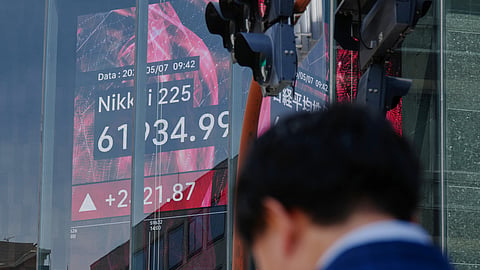 FILE - A person stands in front of an electronic stock board showing Japan's Nikkei index, seen through the glass wall of an office building in Tokyo, May 7, 2026