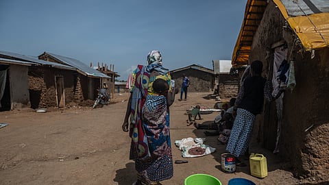 A woman carrying a child walks through the camp on the property of the city's ISP (Institut Supérieur Pédagogique), where internally displaced people reside in Bunia, Congo, Tuesday, May 26, 2026.