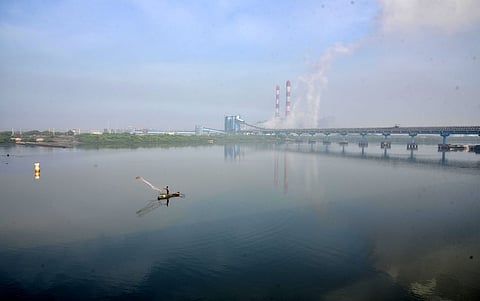 A fisherman casts his net in the waters off Ennore as plumes of smoke rise from a thermal power plant in Chennai.