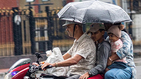 A family rides through rain under an umbrella in Jayanagar, Bengaluru on Sunday.