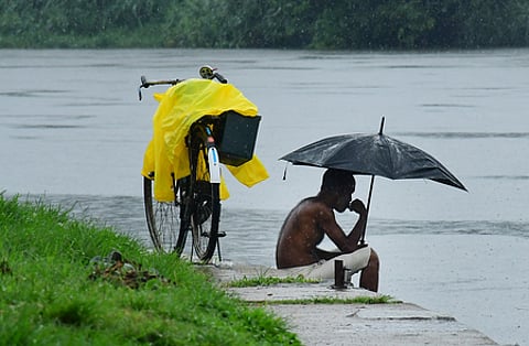 A regular visitor to the Periyar River at Aluva Manappuram sits under an umbrella on the riverbank as rain showers