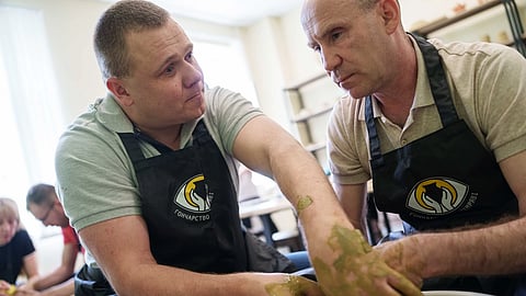 Ivan Shostak, left, a blind Ukrainian war veteran trains his blind comrade Viacheslav Sadovskyi, right, to make a clay plate on a pottery wheel in a workshop at a rehabilitation center in Vinnytsia, Ukraine, on May 21, 2026.