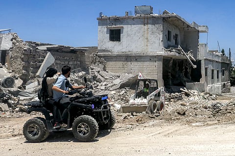 People ride an all-terrain vehicle (ATV) moving past destroyed buildings in the village of Deir Qanoun al-Nahr in southern Lebanon on June 16, 2026.
