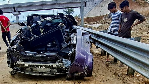 People stand near wreckage of a BMW car after it crashed into a road divider and overturned multiple times, killing at least two persons and injuring another, on the Mumbai-Vadodara highway near Badlapur, in Thane district, Maharashtra, Sunday, June 21, 2026.