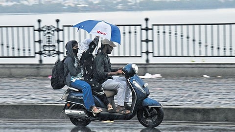 Motorists use an umbrella to shield themselves from rain at Tank Bund in Hyderabad on Sunday.