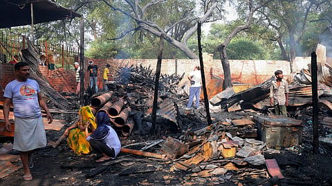 Charred remains at the site as locals gather after a fire broke out in slums behind Maulana Azad Medical College in Balmiki Basti area of Takia Kale Khan, in New Delhi, Tuesday, June 23, 2026.