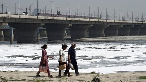 Thick, toxic foam drifts across the surface of the Yamuna River at Kalindi Kunj ghats, caused by untreated sewage and industrial pollution.