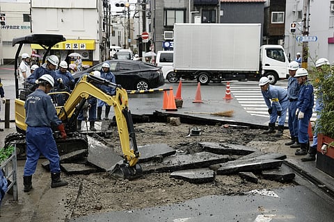 City workers repair a road damaged by water from a manhole following heavy rain, in Osaka, western Japan, Friday, June 26, 2026.