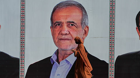 A woman walks past a welcoming billboard featuring Iranian President Masoud Pezeshkian along a roadside in Islamabad, Pakistan, Tuesday, June 23, 2026.