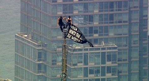 Two people stand on the tip of the antenna of the Empire State Building in New York while holding a banner on Wednesday, July 1, 2026
