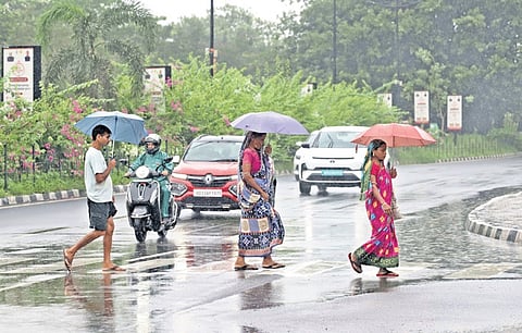 People cross the road holding umbrellas while vehicles pass by, amid heavy rainfall in Bhubaneswar on Saturday