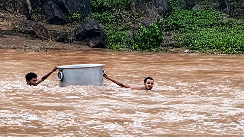Two villagers crossing the swollen Bagh river with the help of an aluminium tope.