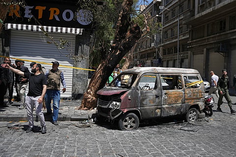 Syrian security personnel inspect a burned vehicle near the Four Seasons Hotel after two explosions rocked the area earlier while Syrian President Ahmad al-Sharaa was meeting French President Emmanuel Macron at the presidential palace, in Damascus, Syria, Tuesday, July 7, 2026.