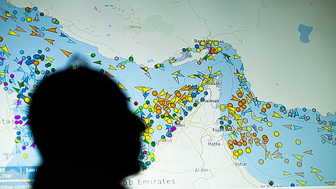 A photo illustration from May 4, 2026, shows a person in front of a large screen displaying vessel movements in the Strait of Hormuz on a ship-tracking website.