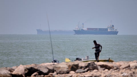 A man stands beside a fishing pole along the shore as cargo ships and commercial vessels are seen in the Strait of Hormuz off Bandar Abbas, Iran, Wednesday, June 17, 2026.