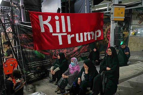 Women sit beneath a banner reading in English, "Kill Trump," during a pro-government rally in Tehran, Friday, July 17, 2026.