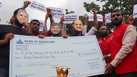 BNP members stage a satirical felicitation for former CMs Siddaramaiah and Basavaraj Bommai, and Chief Minister DK Shivakumar during a protest at Freedom Park on Saturday.
