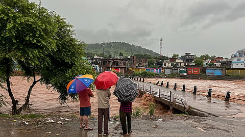 People watch the swollen Mendhar river flowing above the danger level following heavy rains, in Mendhar, Poonch district, Jammu and Kashmir, Monday, July 20, 2026.