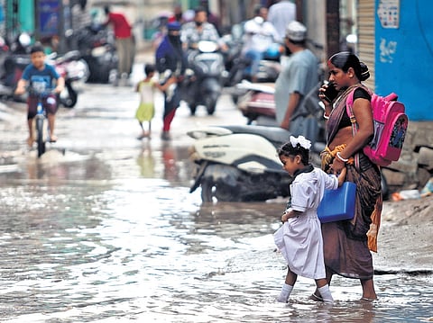 A woman, along with her daughter, walks through a waterlogged street at MS Maktha after sudden rains in Hyderabad on Thursday, July 23, 2026.