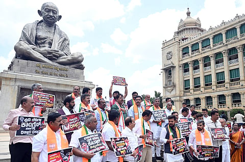 BJP Leaders and Workers protest near Gandhi Statue at Vidhna Soudha on Thursday holding placards reading Goonds Congress Dihkkara in Bengaluru.