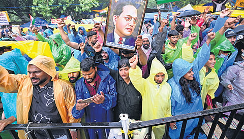 Raincoat-clad supporters brave rain and carry portraits of B R Ambedkar at the protest site on Friday, July 25, 2026.