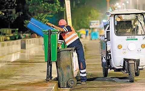 A worker dumping waste in the bin by the roadside in the wee hours |